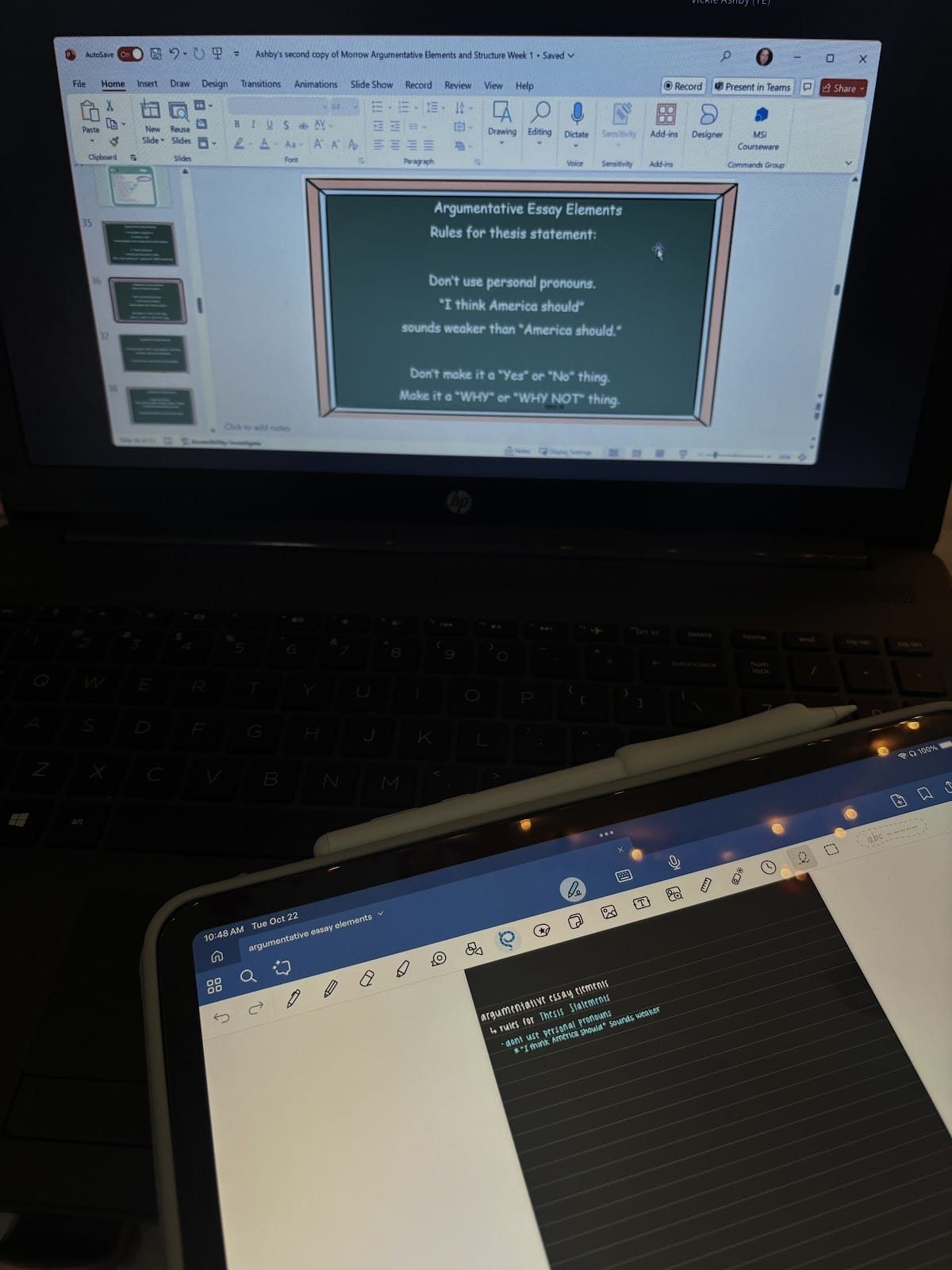 Ein Laptop und ein Tablet mit Notizen für einen argumentativen Aufsatz. Auf dem Laptop-Bildschirm ist eine PowerPoint-Folie mit dem Titel "Argumentative Essay Elements" (Elemente eines argumentativen Aufsatzes) zu sehen, die Regeln für Thesen aufzeigt. Auf dem Tablet werden handschriftliche Notizen zum selben Thema angezeigt.