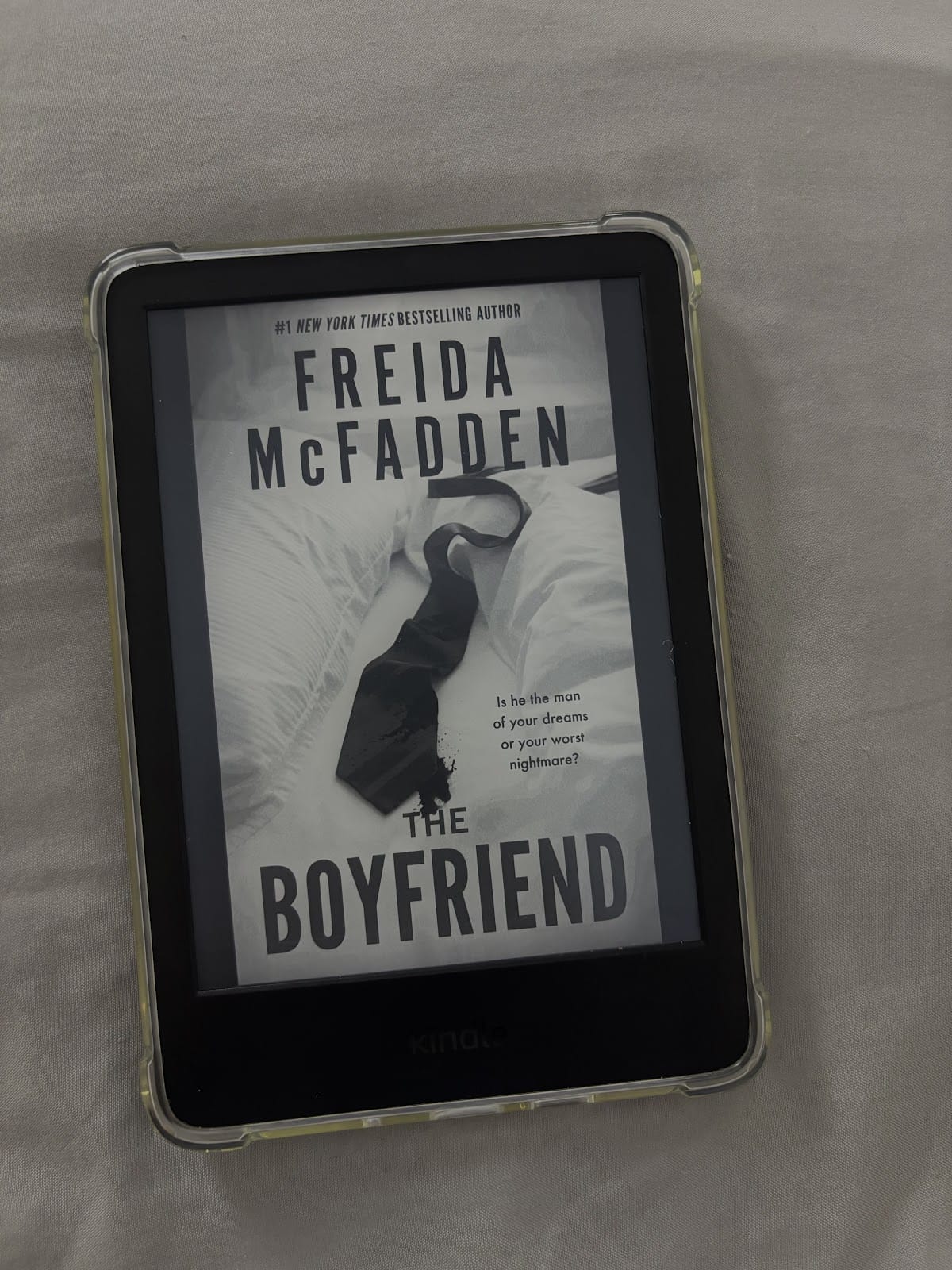 Ein Kindle E-Reader, der das Cover des Buches "The Boyfriend" von Freida McFadden anzeigt. Das Cover zeigt eine schwarze Krawatte auf einer weißen Bettdecke mit dem Text "Ist er der Mann deiner Träume oder dein schlimmster Albtraum?