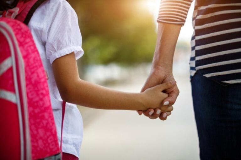 Eine Frau hält sanft die Hand eines Kindes und symbolisiert damit die Liebe und die Verbindung zwischen den beiden.