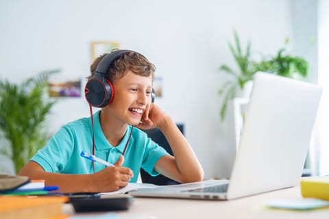 Ein Junge mit Kopfhörern sitzt an einem Schreibtisch, konzentriert auf seinen Laptop, vertieft in seine Arbeit oder Unterhaltung.