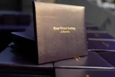 Ein Stapel dunkler Diplomhüllen mit der goldenen Aufschrift "Texas Virtual Academy at Hallsville" als Symbol für Abschluss und Leistung.